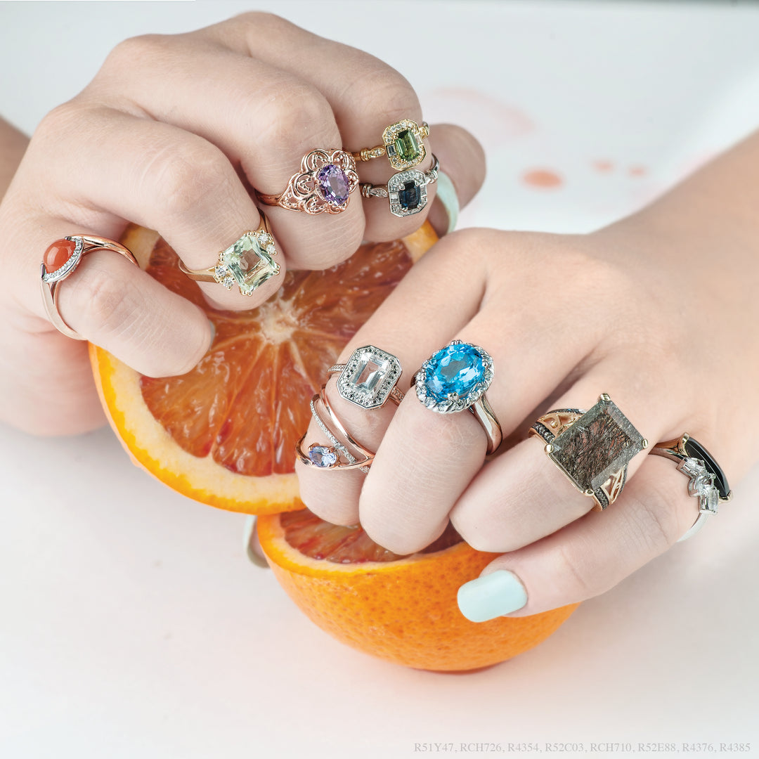 many coloured stone rings is assorted shapes stacked on every finger of the model's hand, image features black onyx, blue topaz, peridot, lilac amethyst, sapphires